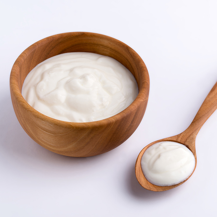 White yogurt in natural wooden bowl with wooden spoon.
